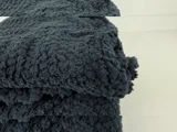 Et nærbillede af et foldet, mørkegråt, luftigt tæppe med en blød, struktureret overflade, placeret på en lys overflade.
