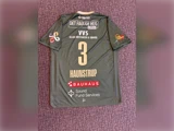 En grøn sportstrøje med nummer 3 og navnet Haunstrup på ryggen, med flere sponsorlogoer på en mønstret lilla baggrund.