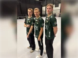 Tre mænd står inde på et gymnastiksalsgulv iført ens mørkegrønne sportstrøjer og sorte bukser og poserer for kameraet.