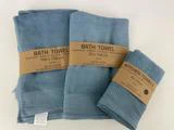 Tre blå håndklæder i forskellige størrelser, mærket som badehåndklæder og køkkenhåndklæder, hver med brune papirbånd, der viser deres størrelse og materialesammensætning.