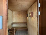 Et saunarum i træ med to bænkeniveauer langs væggene, et flisegulv og lamelbelysning i træ på væggen.