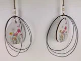 To ovale hængende ornamenter med malede vilde blomster og sommerfugle, dekoreret med sorte trådløkker og træperler, vist mod en struktureret hvid baggrund.
