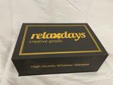 En sort æske med guldbogstaver, hvor der står relaxdays creative goods på låget og High Quality Whiskey Glasses på siden, placeret på en hvid stofoverflade.