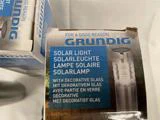 Nærbillede af en Grundig solcelleboks med produktnavn på flere sprog og et billede af solcellelampen med dekorativt glas.