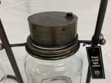 En glaskrukke med metallåg, der er fastgjort til et stativ, med et mærke, hvor der står: There is LED light inside!.