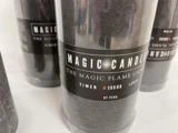 Nærbillede af et sort stearinlys mærket MAGIC CANDLE, THE MAGIC FLAME CANDLE, TIMER 360HR, BY PEHA med andre lignende stearinlys i baggrunden.