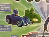 To legetøjsbiler, en blå med en Catboy-figur mærket Cat-Car og en grøn med en Gekko-figur mærket Gekko-Mobile, på en grøn baggrund.
