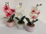 Tre kunstige orkidéer i potter - pink, hvid og hvid med pink midte - er arrangeret i dekorative potter med et struktureret, gitterlignende design på en hvid baggrund.