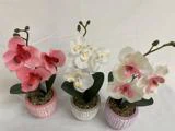 Tre kunstige orkidéer i potte med rosa, hvide og lyserøde blomster, placeret side om side på en hvid baggrund.