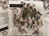 En pakke ARTSTYLE-servietter med illustrerede hunde i forskelligt tøj, bl.a. jakker, hatte og bandanaer, der poserer sammen i en gruppe.