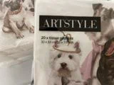 En pakke ARTSTYLE-servietter med illustrationer af hunde, bl.a. en hvid hund med en lille festhat. Teksten lyder som følger: 20 x stofservietter 33 x 33 cm/13 x 13 tommer.