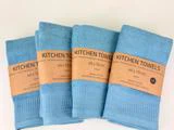 Fire foldede blå køkkenhåndklæder med strukturerede mønstre, hver indpakket i en brun etiket med teksten KITCHEN TOWELS, 40 x 70 cm, 80 % bomuld, 20 % viskose & lyocell.