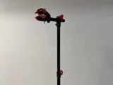 Et sort stativ med røde klemmer og justeringsknapper, opstillet mod en almindelig lys væg.