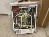 Et indpakket gennemsigtigt drivhuscover med et foto af et lille hvidt trædrivhus med planter indeni. På etiketten står målene 81x61x122 cm og mærket EST WOOD.