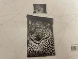 Et sengesæt med et realistisk sort-hvidt leopardprint består af et pudebetræk og et dynebetræk på en geometrisk mønstret baggrund.