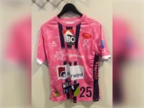 Lyserød kortærmet sportstrøje med sorte detaljer og forskellige sponsorlogoer, med nummeret 25 nederst på forsiden.
