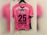 Bagside af en lyserød fodboldtrøje med nummeret 25 og navnet LYNNERUP trykt på ryggen samt forskellige sponsorlogoer.