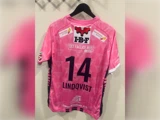 En lyserød sportstrøje med nummer 14, navnet LINDQVIST og forskellige sponsorlogoer på ryggen, hængende på en bøjle.