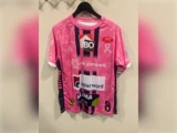 En lyserød fodboldtrøje med lodrette marineblå striber og flere sponsorlogoer, med nummer 8 på ryggen.
