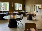 En moderne, elegant restaurantspisestue med runde borde, moderne stole, opdækning, store vinduer og naturligt lys.