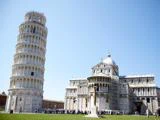Det skæve tårn i Pisa og katedralen i Pisa i Italien, med en klar blå himmel og grupper af turister samlet omkring vartegnene.