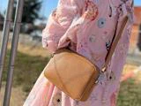 En person i en pink kjole med muslingemønster bærer en lysebrun crossbody-taske med struktur udendørs.