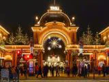 Feststemte mennesker samles ved den oplyste indgang til Tivoli i København, der er udsmykket med julelys, træer og dekorationer om aftenen.