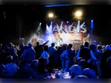 Et liveband optræder på scenen i lyset fra KANDIS, mens publikum ser på, og nogle danser foran scenen.
