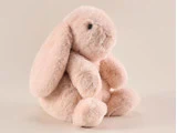En blød, lyserød kanin i plys med lange hængeører sidder oprejst på en almindelig beige baggrund.