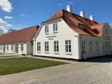 En hvid bygning med rødt tegltag og et skilt med teksten Kongenshus Hotel under en blå himmel med spredte skyer.