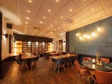 Et moderne restaurantinteriør med træborde, -stole og en unik baggrundsbelyst hyldeudstilling.