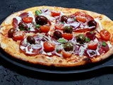 En pizza toppet med salami, oliven, cherrytomater, rødløg og hvid sauce.