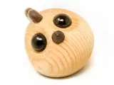 En lille, rund trægenstand med to store sorte øjne og to små ører, der ligner et abstrakt dyr, på en hvid baggrund.