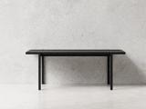 Et minimalistisk sort rektangulært bord med rene linjer står mod en almindelig lysegrå struktureret væg og et glat hvidt gulv.