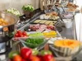 En morgenmadsbuffet med forskelligt pålæg, oste, skiveskårne grøntsager, frugt og skåle med smørepålæg arrangeret på en disk.