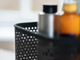 Nærbillede af en sort, perforeret beholder med flasker, bl.a. en sølvfarvet og en ravfarvet, med sløret baggrund.