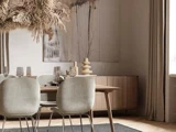En moderne spisestue med træbord, lysegrå stole, lysekrone med tørrede blomster, abstrakt vægkunst og indretning i neutrale toner.