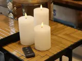Tre hvide flammeløse LED-søjlelys med realistiske flammer står på et træbord ved siden af en sort fjernbetjening.
