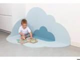 En baby sidder på en skyformet blå måtte i hjørnet og leger med en åben bog eller et stykke legetøj på gulvet.