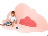 Et lille barn sidder på en lyserød, skyformet legemåtte og leger med legetøjsbiler af træ og en lastbil.
