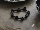 Et sort, sekskantet objekt med seks runde åbninger hviler på en betonflade ved siden af mønstrede skåle og spredte kviste.