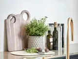 Skærebrætter, en potteplante, to flasker olie, kogebøger og figner er arrangeret pænt på køkkenbordet.
