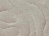 Nærbillede af et beige, struktureret stof med bløde, bølgede syninger, der ligner quiltet eller polstret betræk.