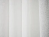 Nærbillede af hvide gardiner, der hænger i bløde folder, så lyset forsigtigt filtreres gennem stoffet.