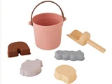 En pink spand med håndtag, en gul skovl og fire sandforme formet som en regnbue, en bjørn, en bil og en sol, alt sammen arrangeret på en hvid baggrund.