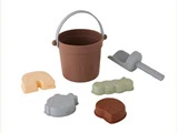 En brun legetøjsspand med et gråt håndtag, en grå legetøjsskovl og fire pastelfarvede sandforme i forskellige former på en hvid baggrund.