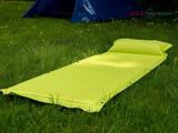 En knaldgul campingmåtte med en tilhørende pude ligger på grønt græs med et blåt telt i baggrunden.