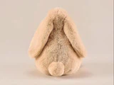 En plysdyrkanin set bagfra, med hængeører og en lille rund hale, lavet af blød beige pels, på en ensfarvet baggrund.