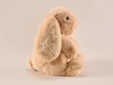En blød, lysebrun kanin i plys med hængeører sidder oprejst på en almindelig, lys baggrund.