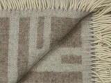 Nærbillede af et beige og brunt vævet tæppe med frynsede kanter, hvor hjørnet er foldet om, så man kan se begge sider af stoffet.